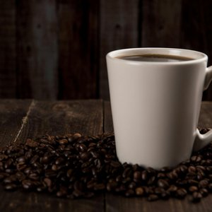 A rustic ceramic mug filled with hot coffee, surrounded by coffee beans on a wooden table.
