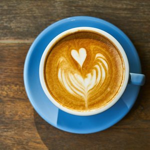 Top view of a latte with heart art in a blue cup on a wooden table.