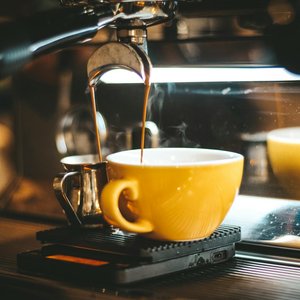Steaming espresso pours into a yellow cup in a cozy café.