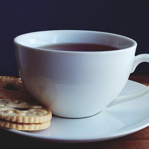 A white cup of tea with biscuits on a wooden table. Perfect for tea time concepts.