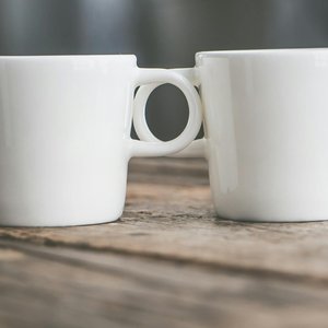 Two connected white ceramic cups on a rustic wooden surface, showcasing depth of field.