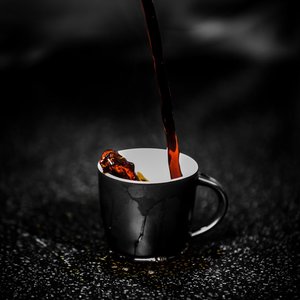 Close-up of steaming dark coffee being poured into a black cup on a dark textured surface. Rich aroma.