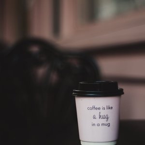 A takeaway coffee cup with a warm inspirational quote on a wooden surface.