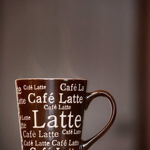A close-up of a steaming café latte in a bold, text-covered mug, perfect for a cozy morning.