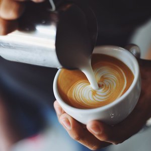 A barista skillfully pours milk into a coffee cup, creating a beautiful latte art swirl.