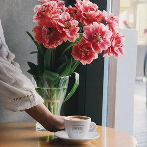 A serene indoor scene with fresh pink tulips in a vase beside a coffee cup on a wooden table.