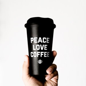 Close-up of a hand holding a coffee cup with 'Peace Love Coffee' text, promoting positivity.