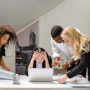 Diverse group of coworkers engaged in a collaborative office meeting, discussing around a laptop.