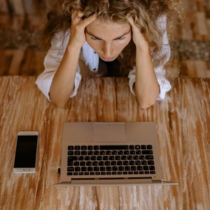 A woman looking stressed while working on a laptop from home, viewed from above.