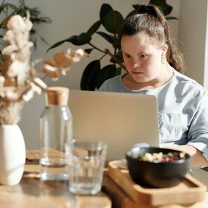 Young woman with Down syndrome using a laptop at a cozy home setting, enjoying leisure time.