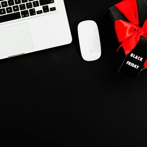 Flat lay of a laptop and Black Friday gift box with red bow, perfect for online shopping themes.