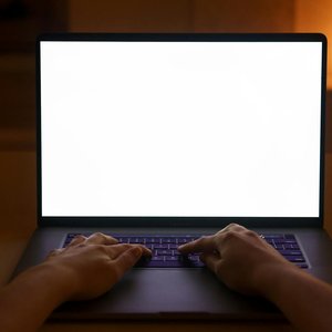 Hands typing on a laptop with a blank screen, creating a cozy and quiet workspace atmosphere indoors.