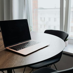 A cozy workspace with a laptop on a wooden table by a window offering natural light.