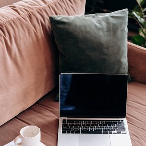 A peaceful home workspace featuring a laptop, coffee, and documents on a sofa, perfect for remote work.