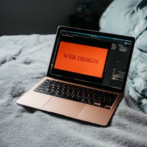 A laptop on a bed showing web design software, creating a cozy workspace.