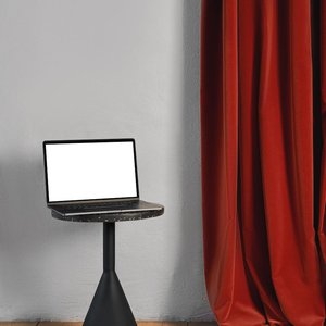 Sleek laptop with blank screen on a table beside a red curtain, ideal for mockups.