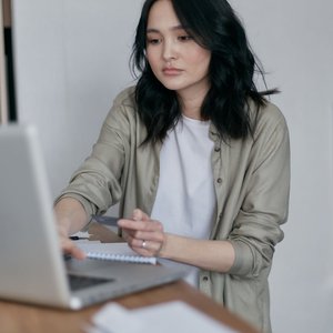 A young adult woman attentively working on her laptop at home, taking notes.
