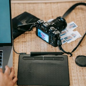 High angle of crop anonymous designer with netbook near graphics tablet and professional photo camera on desk