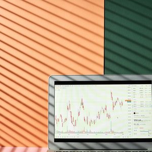 A laptop showing financial graphs with shadow lines against a colorful background, illustrating market analysis.
