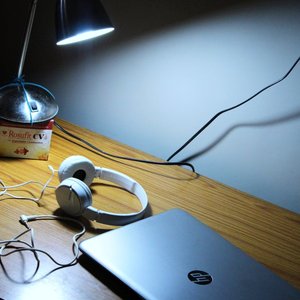 A cozy modern workspace featuring a laptop, headphones, and a lamp on a wooden desk.