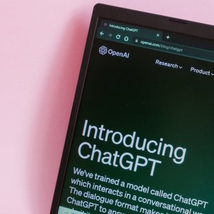 Close-up of a laptop with ChatGPT introduction on screen against a pink background.