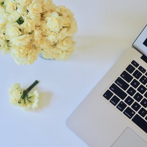 Minimalist workspace with bouquet of flowers and a laptop on a white desk.
