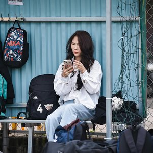 Young woman on a bench with backpacks, focused on her phone outdoors.