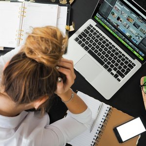 Overhead view of a stressed woman working at a desk with a laptop, phone, and notebooks.