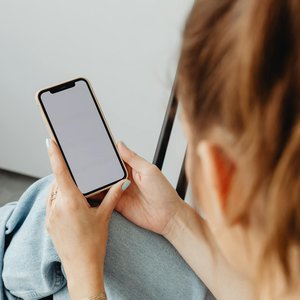 A woman holds a smartphone with a blank screen indoors, offering a mockup opportunity.