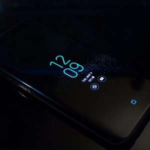Close-up of a smartphone in the dark displaying digital clock and notifications.