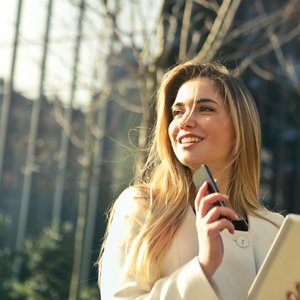 Smiling businesswoman holding smartphone and tablet outdoors in Milan.