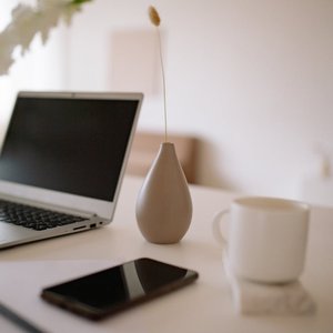 A clean and modern workspace featuring a laptop, vase, cup, smartphone, and paper on a white table.