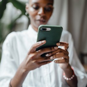 A woman in a white blouse using her smartphone indoors, showing a thoughtful and calm mood.
