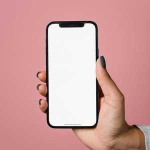 A hand holding a smartphone with a blank screen against a pink background.