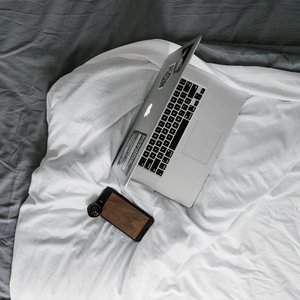 Minimalist overhead view of a laptop and smartphone on a cozy bed, ideal for remote work settings.