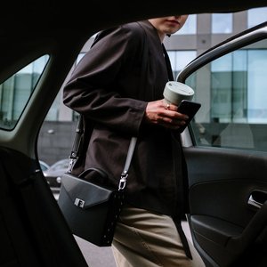 Stylish woman entering a car, holding coffee and smartphone, showcasing urban lifestyle.