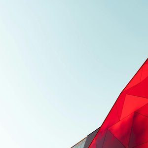A vibrant red geometric facade of a modern building against a clear sky.
