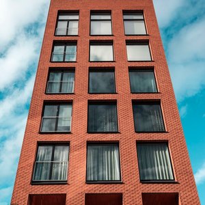 Red-brick modern building against a vibrant blue sky and clouds.