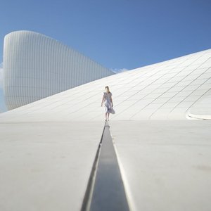 A person gracefully walks on a modern building with sweeping curves under a clear blue sky.