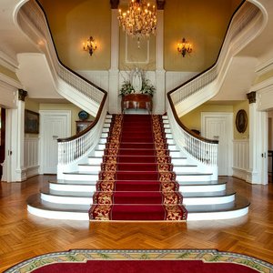 Grand staircase with red carpet in a luxurious hotel lobby, highlighted by a chandelier.