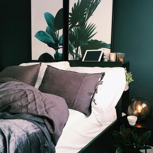 A stylish and cozy bedroom featuring green walls, botanical prints, and soft lighting for a contemporary feel.