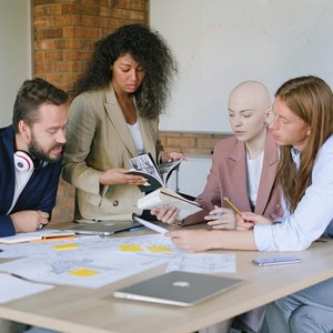 Group of multiracial businesspeople speaking and sharing data about project and analyzing reports in notebooks at table in office