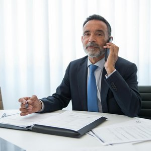 Senior businessman in suit discussing important documents on the phone at an office room.