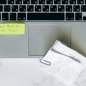 A laptop with a sticky note reminder and receipts, emphasizing tax season organization.