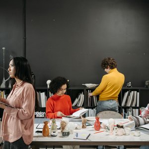 A group of adults engaged in creative work and discussion around a table in an office setting.