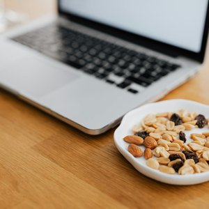 A plate of mixed nuts beside a laptop on a wooden desk, perfect for remote work inspiration.