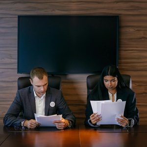 Two professionals reviewing documents at a meeting table in a modern conference room.