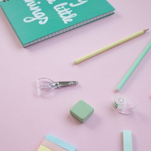 A flat lay of pastel school supplies on a pink surface featuring a notebook and stationery.
