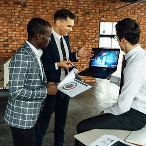 Three business professionals discussing financial charts in a modern office setting.