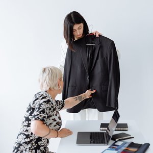 Two women discussing fashion choices with a suit in an office setting.